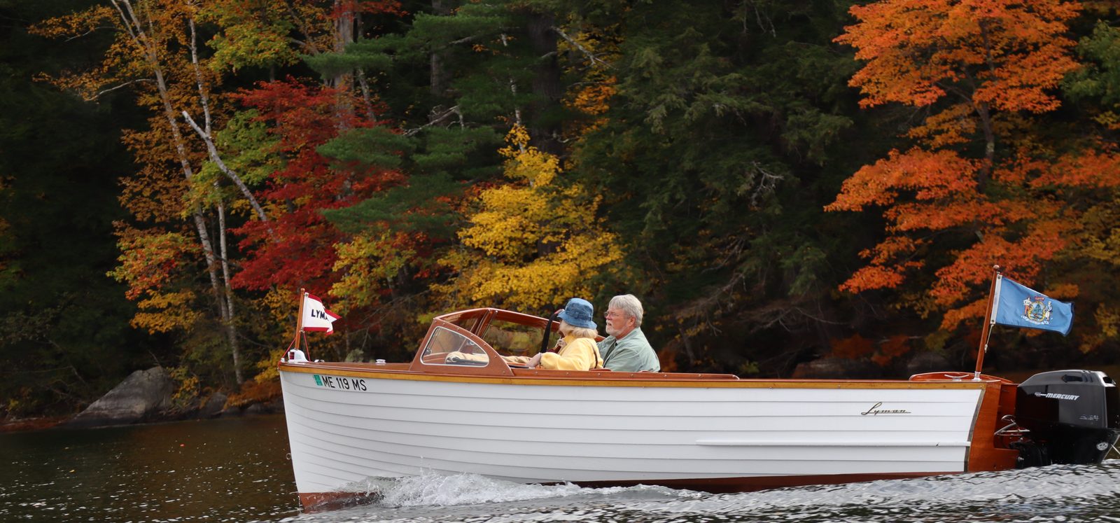 Jeff and Vonla cruising past bright fall foliage in their classic boat