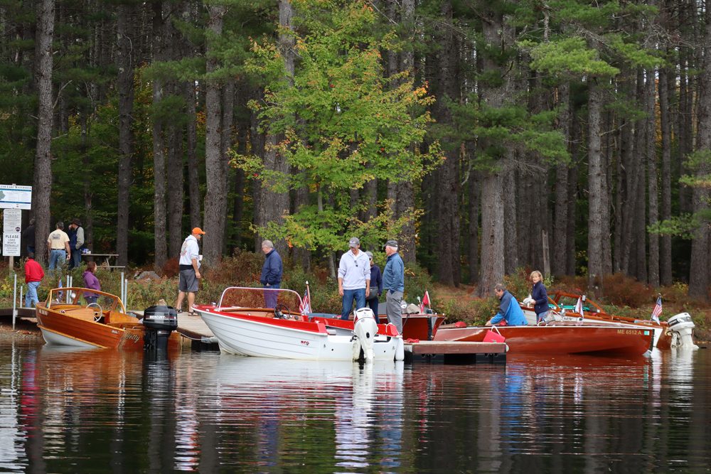 Members gathered on the shore and docks at a launch ramp as classic boats are put in the water